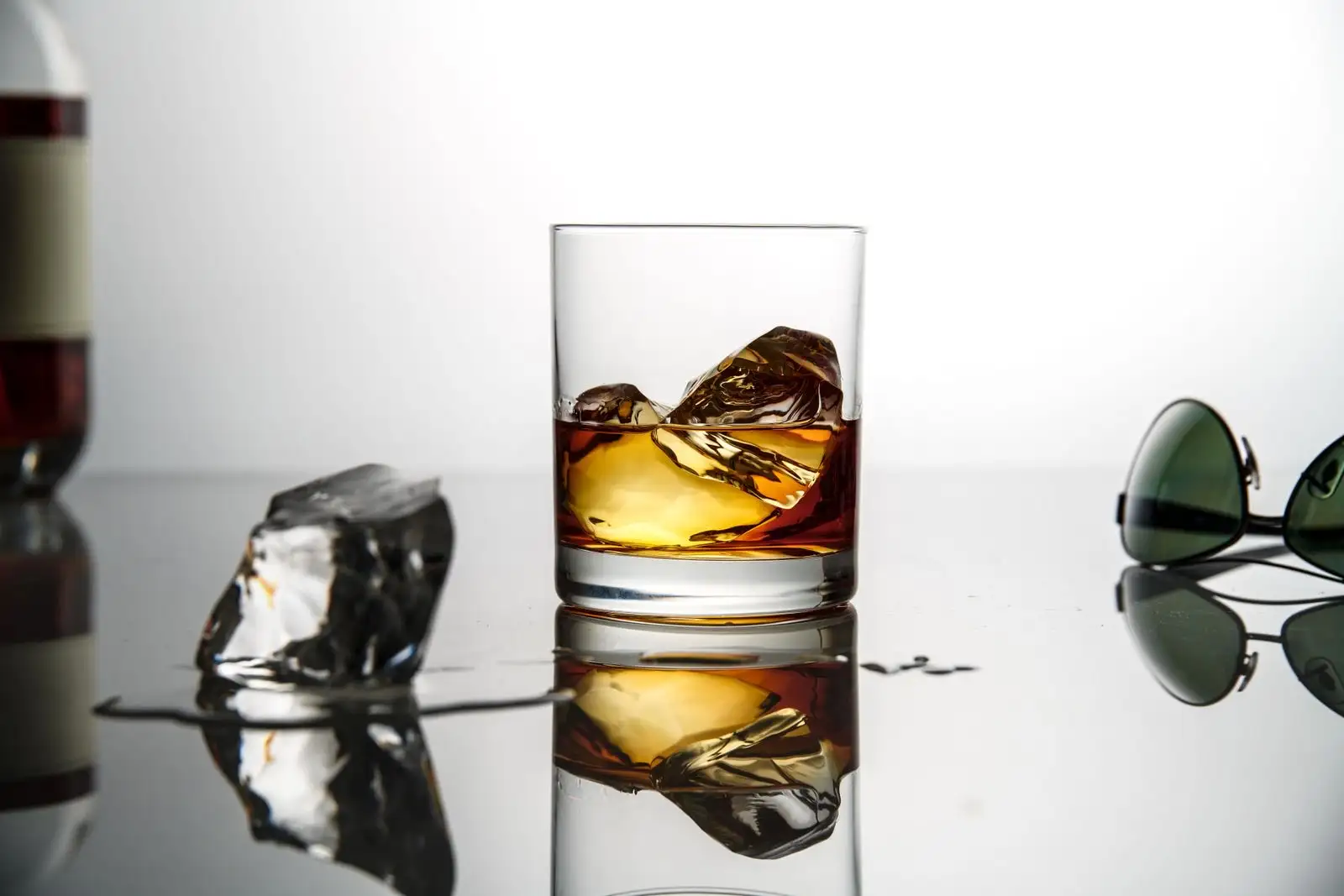 Glass of whisky on ice on a reflective surface, white background