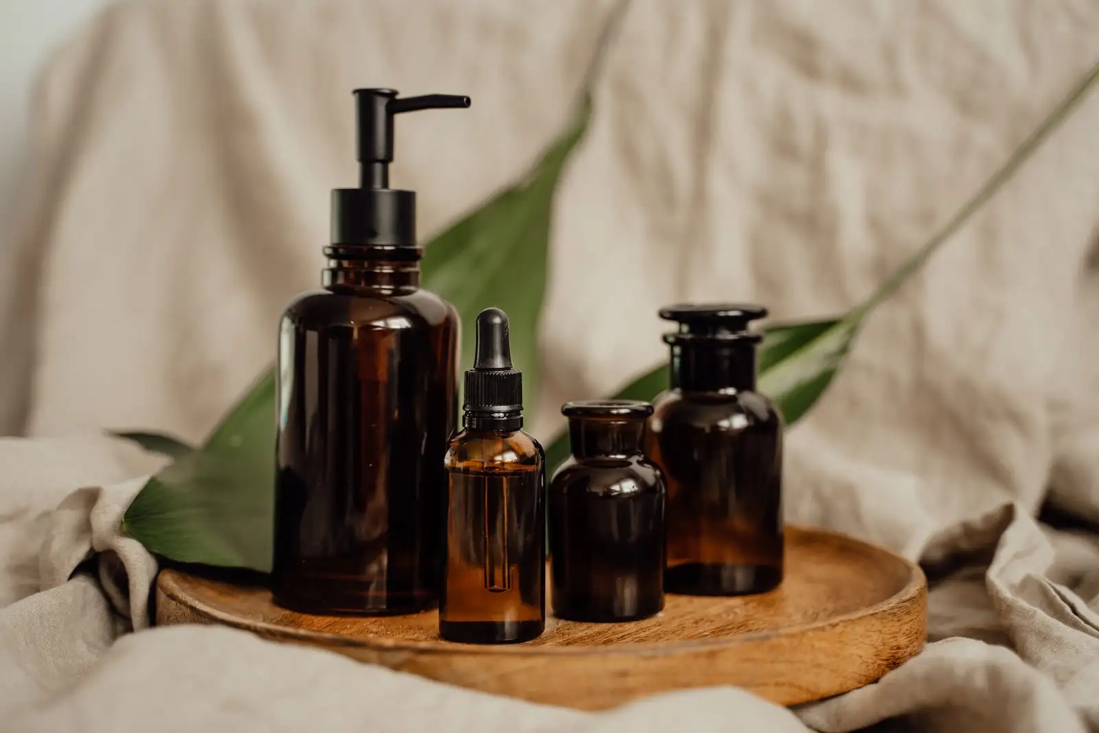 Amber glass cosmetic bottles, including a dropper and a pump bottle, on a wooden tray