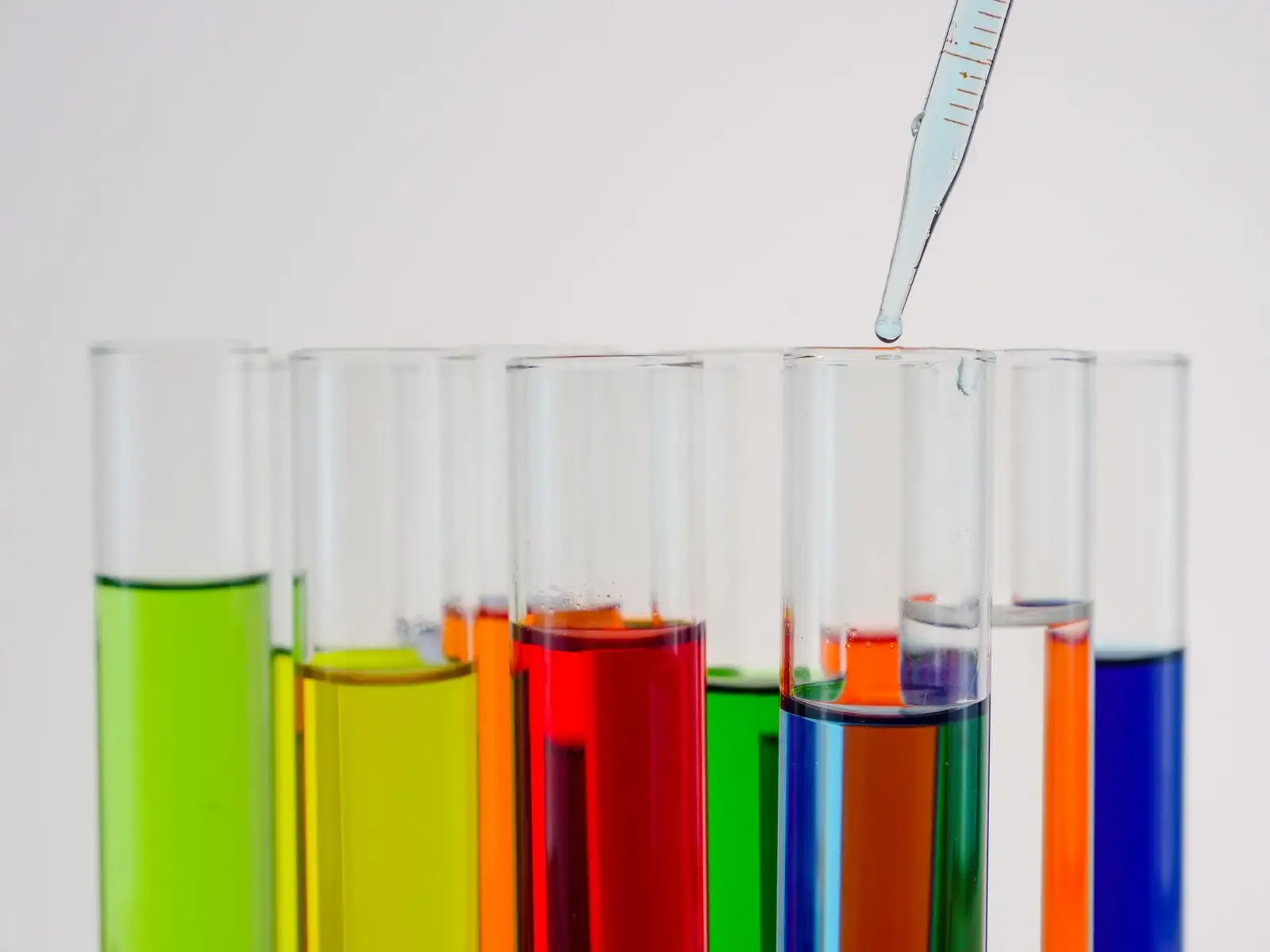 Graduated pipette above a row of test tubes filled with liquids of different colours