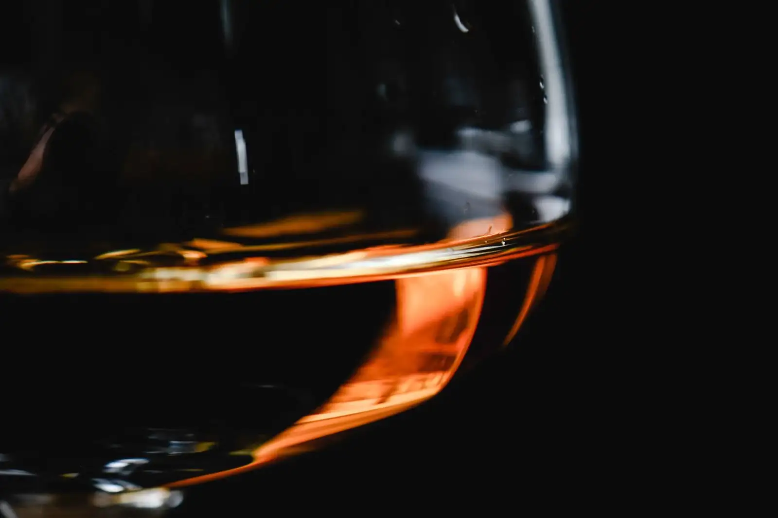 Close-up of a brandy glass, a finger of amber spirit lit against a black background