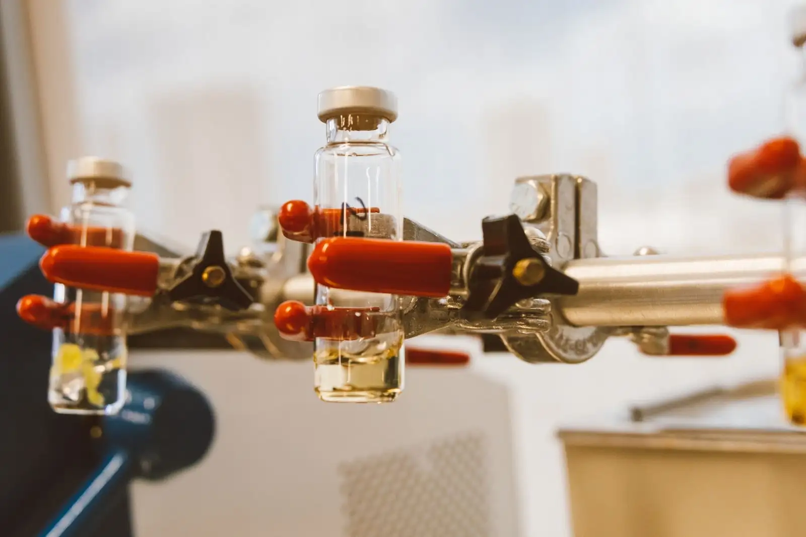 Laboratory vials holding an amber extract, held by clamps on a stand