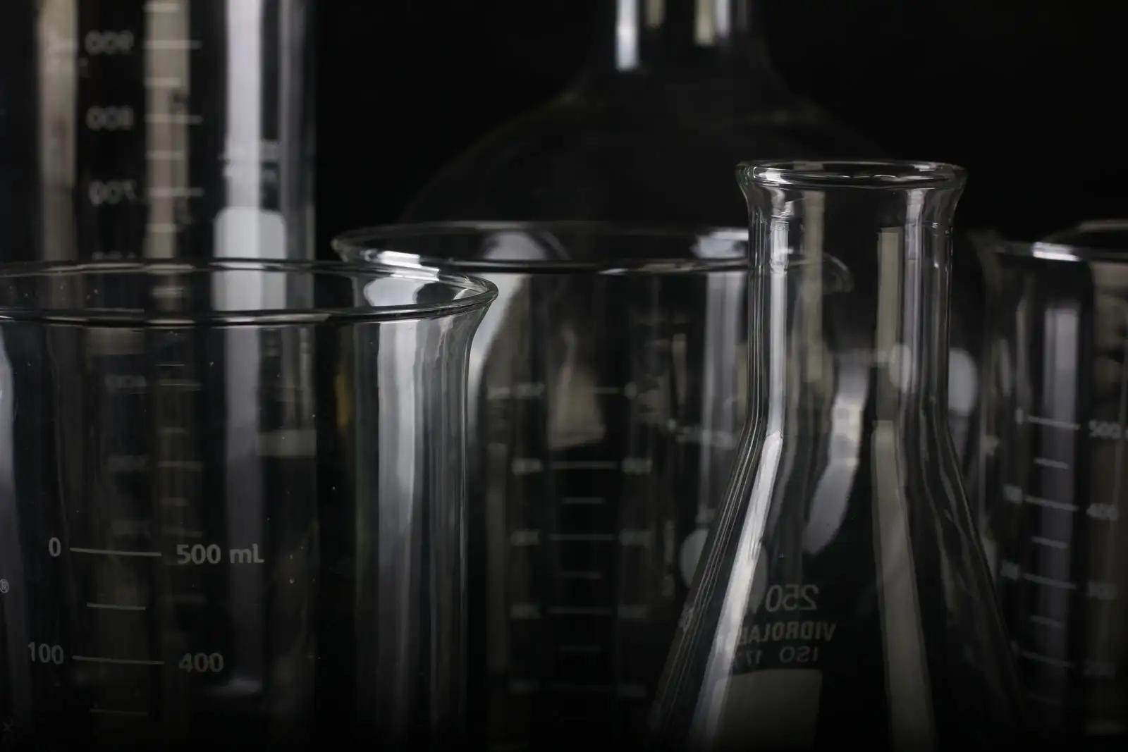 Glass beakers, an Erlenmeyer flask and graduated cylinders against a black background