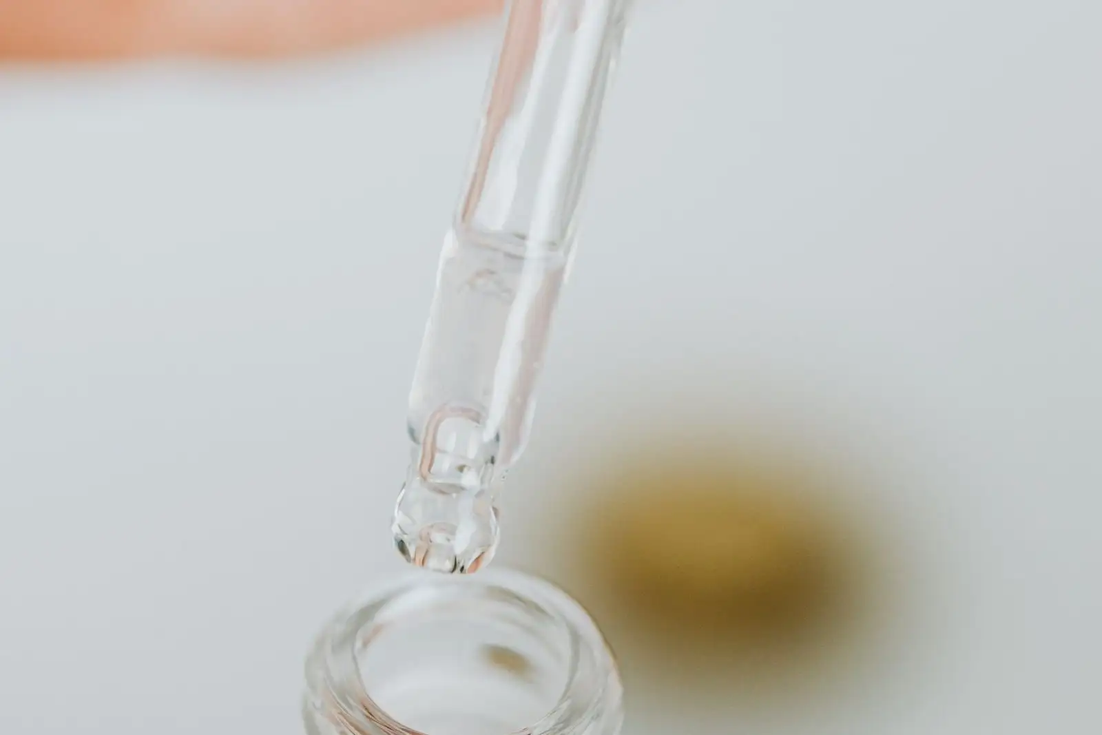 Glass pipette above an open bottle, a drop about to fall