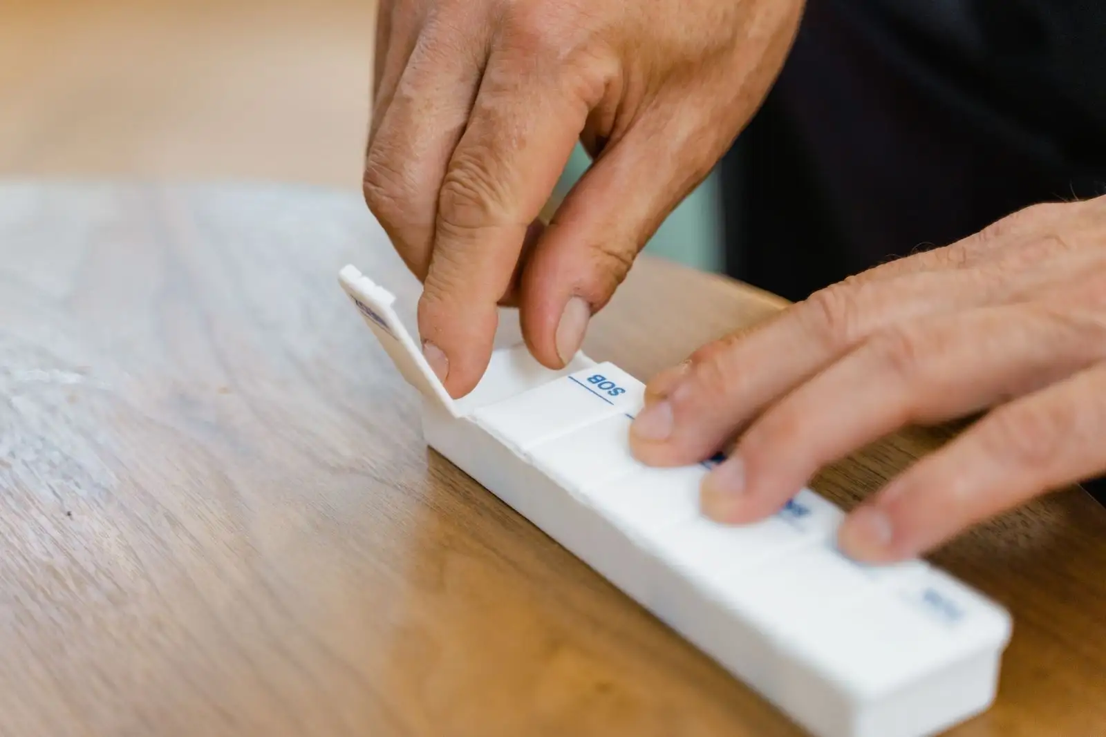 Hands of an older person sorting medicines into a weekly pill organiser on a wooden table