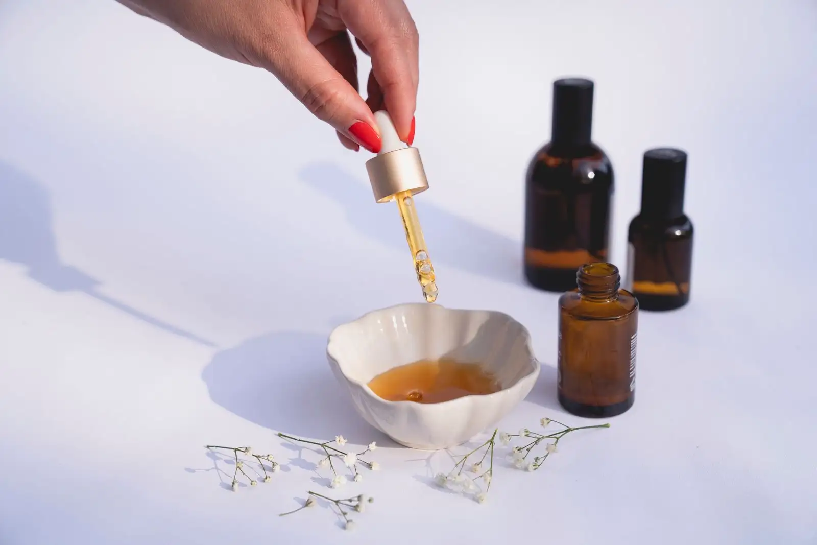 Glass pipette dripping amber oil into a small white dish, next to brown glass bottles