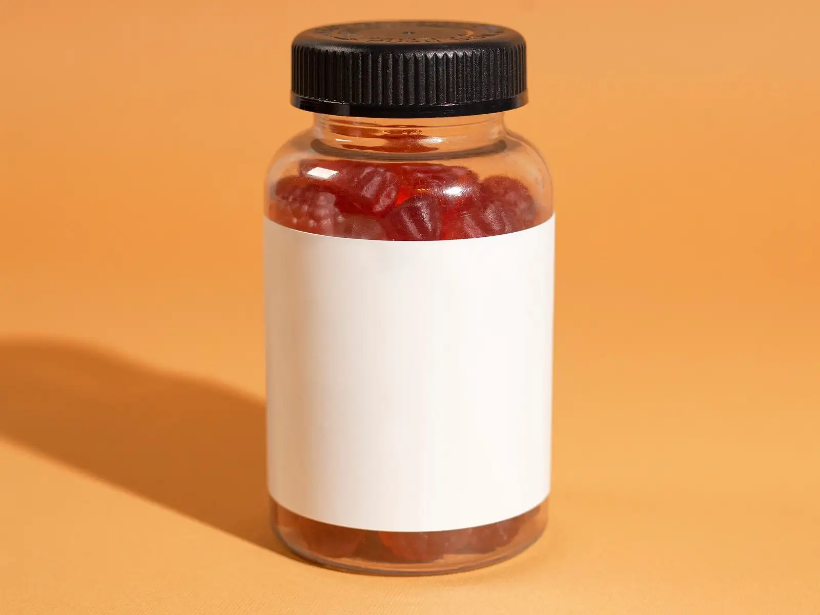 Clear jar filled with red gummies, blank label, on an orange background