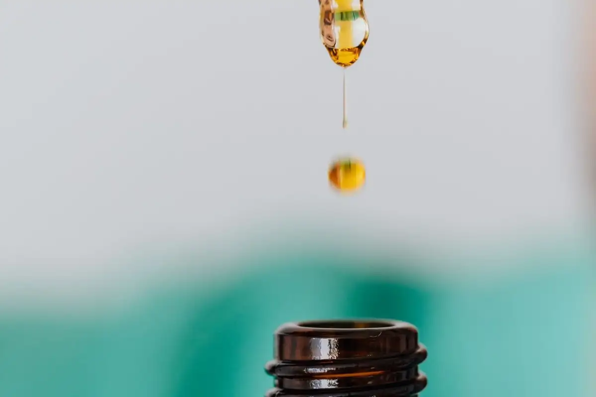 A drop of amber oil falls from a pipette above a brown glass bottle