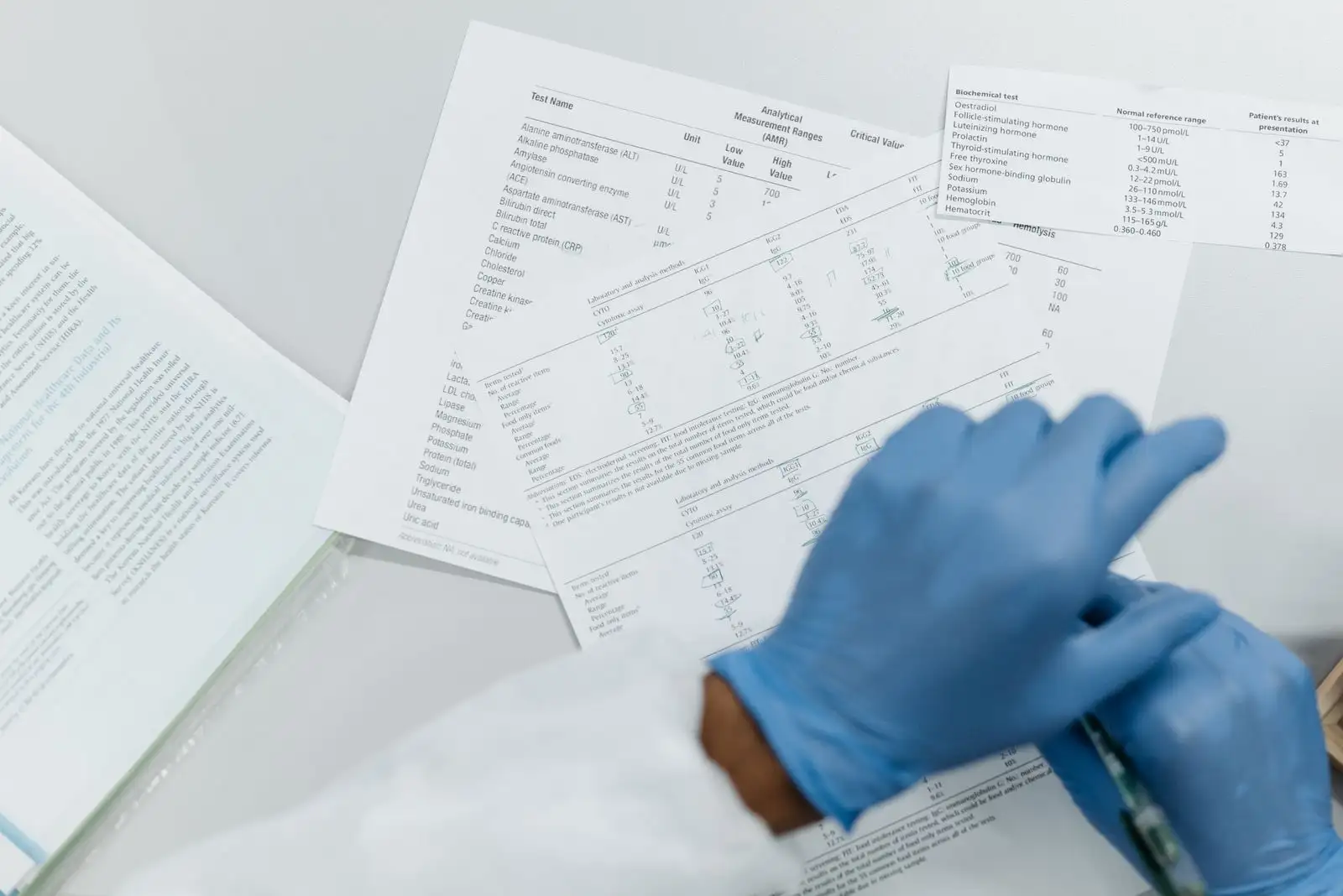 Gloved hands reviewing printed laboratory test results, tables of values on a white desk