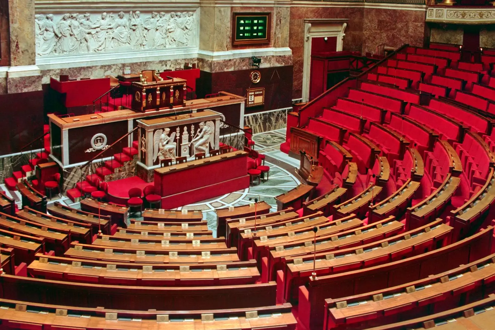 The empty chamber of the French National Assembly, rows of red seats facing the rostrum