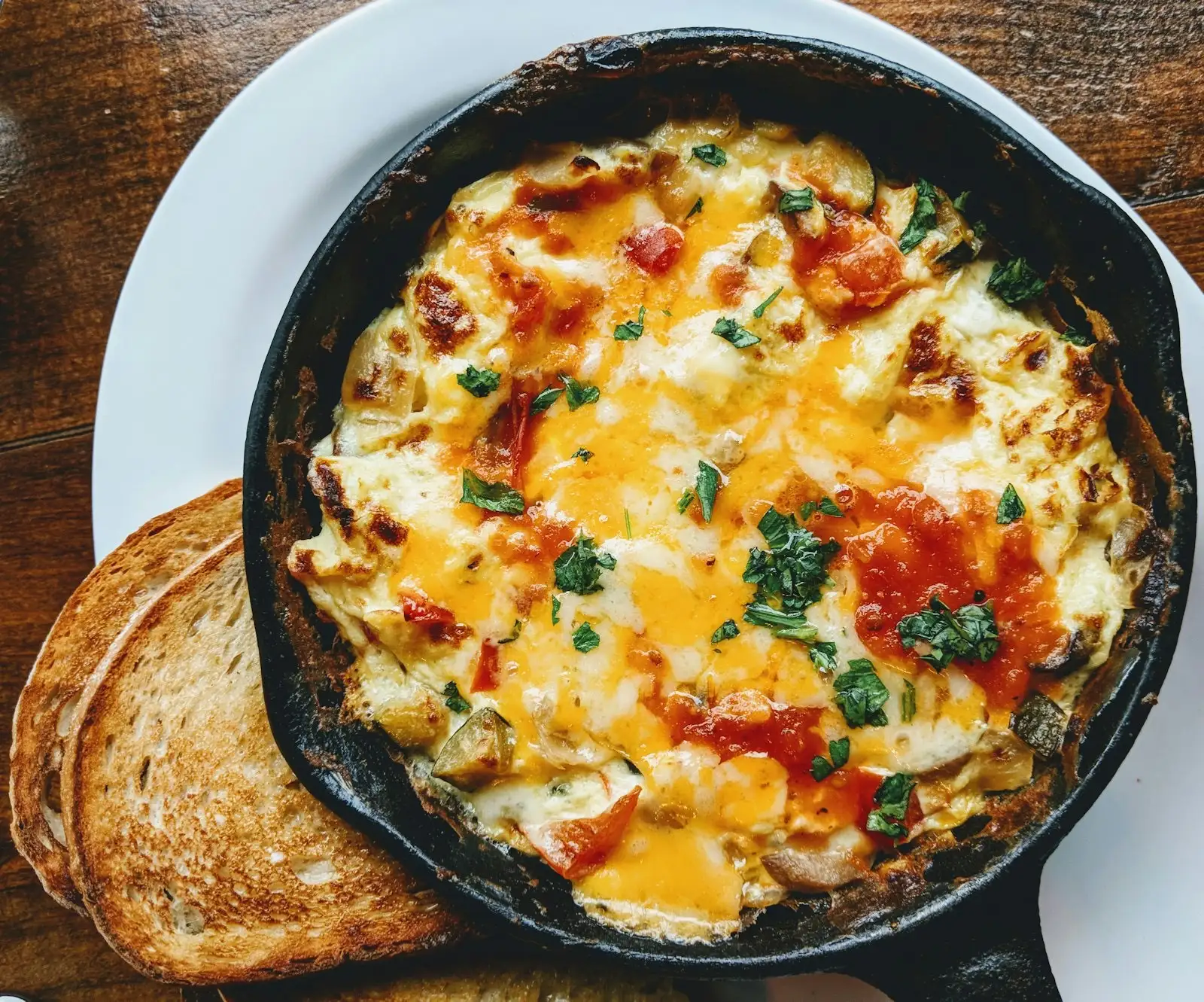 Baked omelette with tomatoes and parsley in a small cast-iron pan, served with two slices of toast