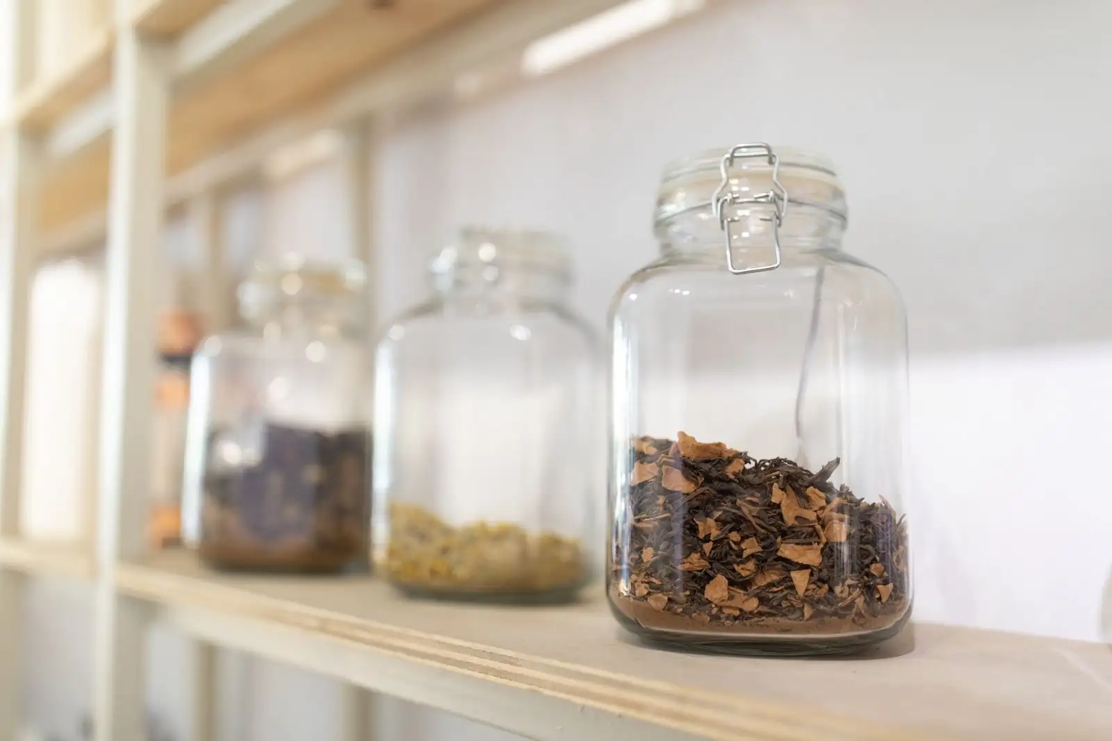 Glass jars filled with dried plants lined up on a wooden shelf