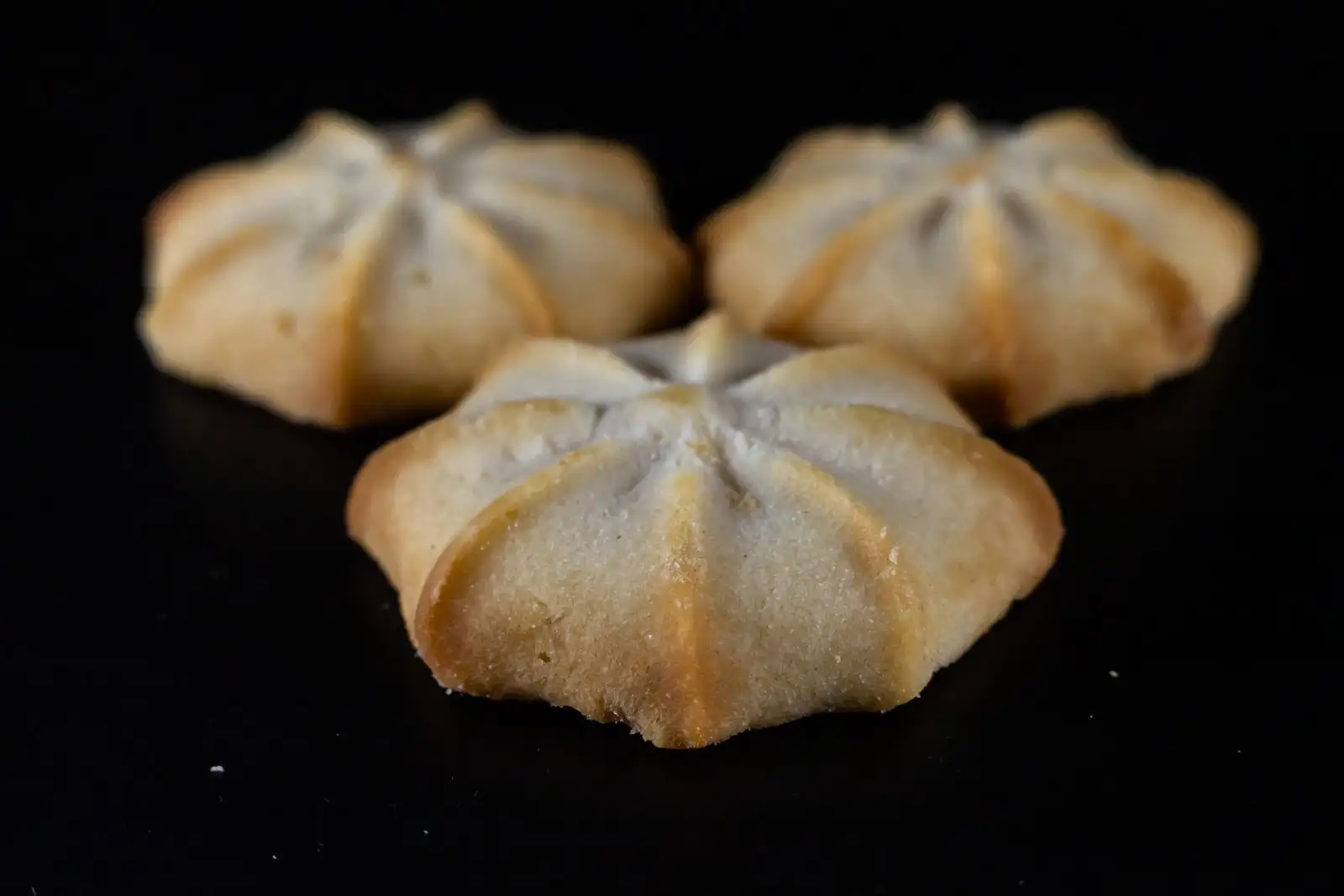 Three golden rosette-shaped shortbread biscuits on a black background