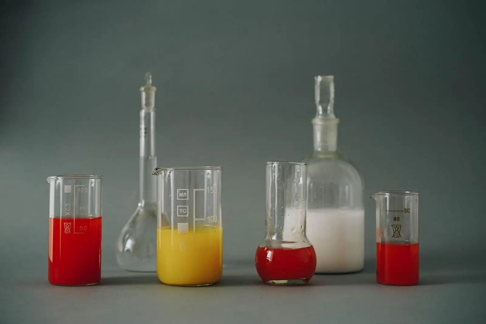 Laboratory beakers and flasks filled with red, yellow and white liquids on a grey background