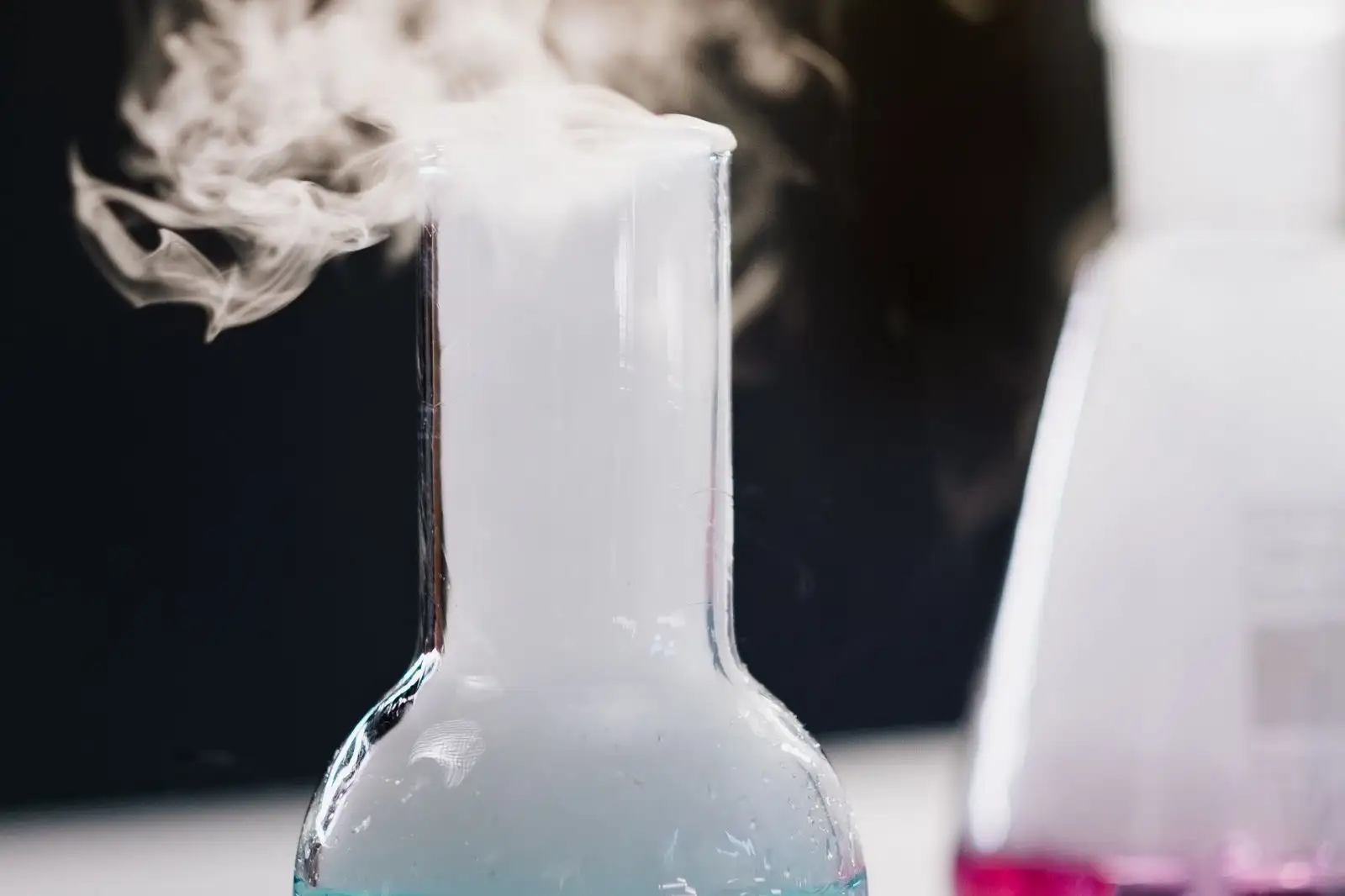 Laboratory flask releasing white vapour against a dark background