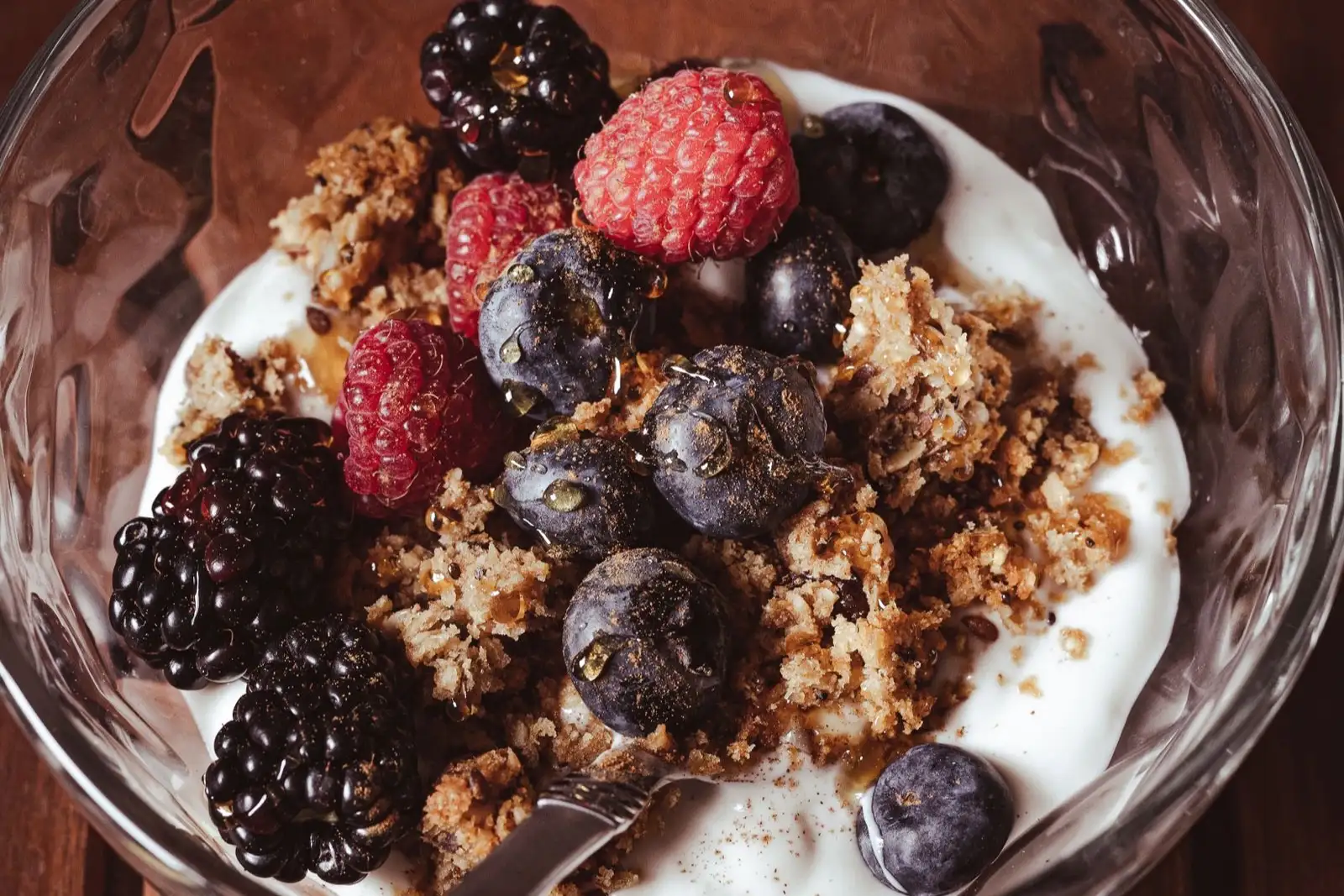 Bowl of thick yogurt topped with granola, blackberries, raspberries and blueberries, with a spoon in it