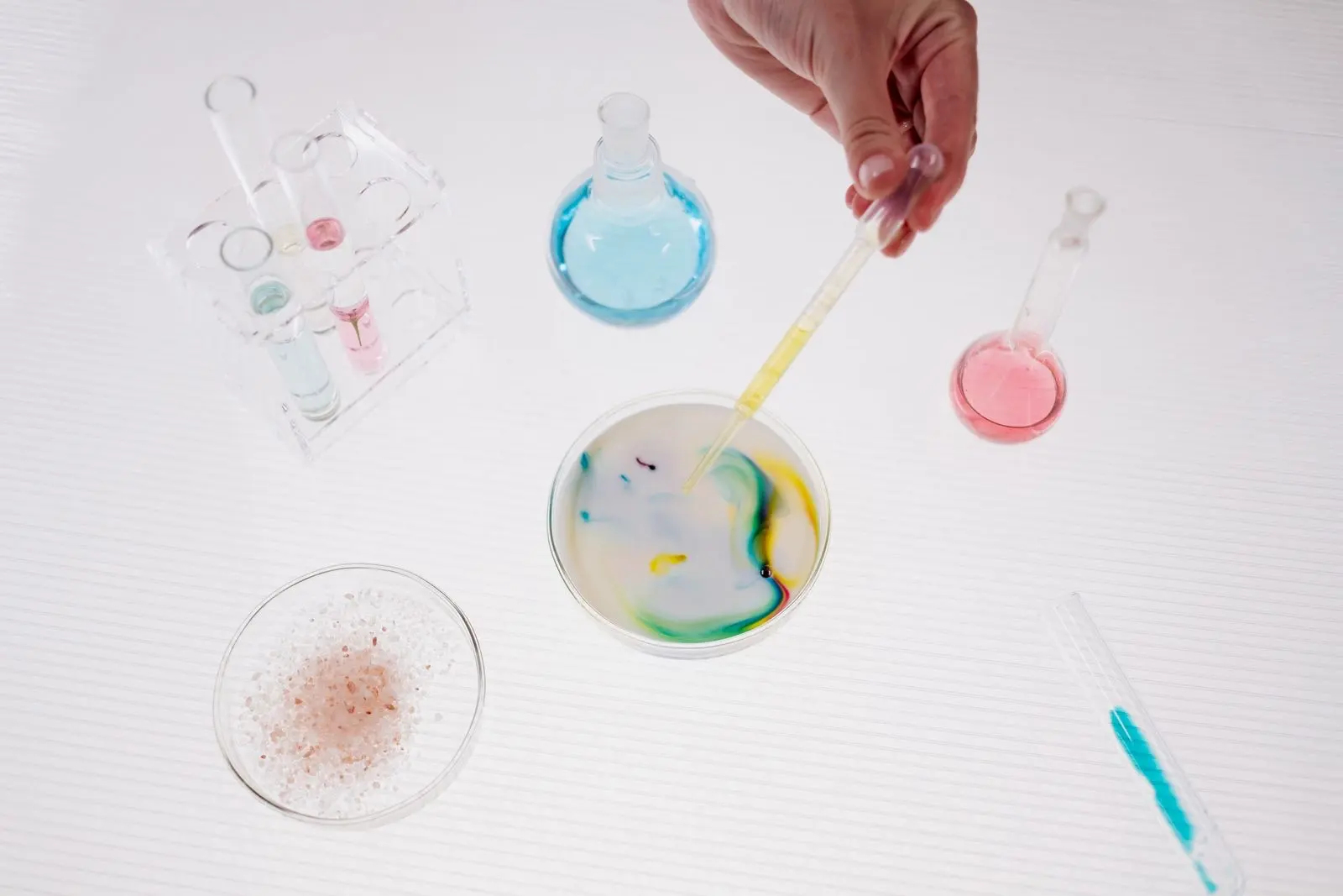 Pipette dropping liquid into a Petri dish filled with a white emulsion, among lab flasks and tubes