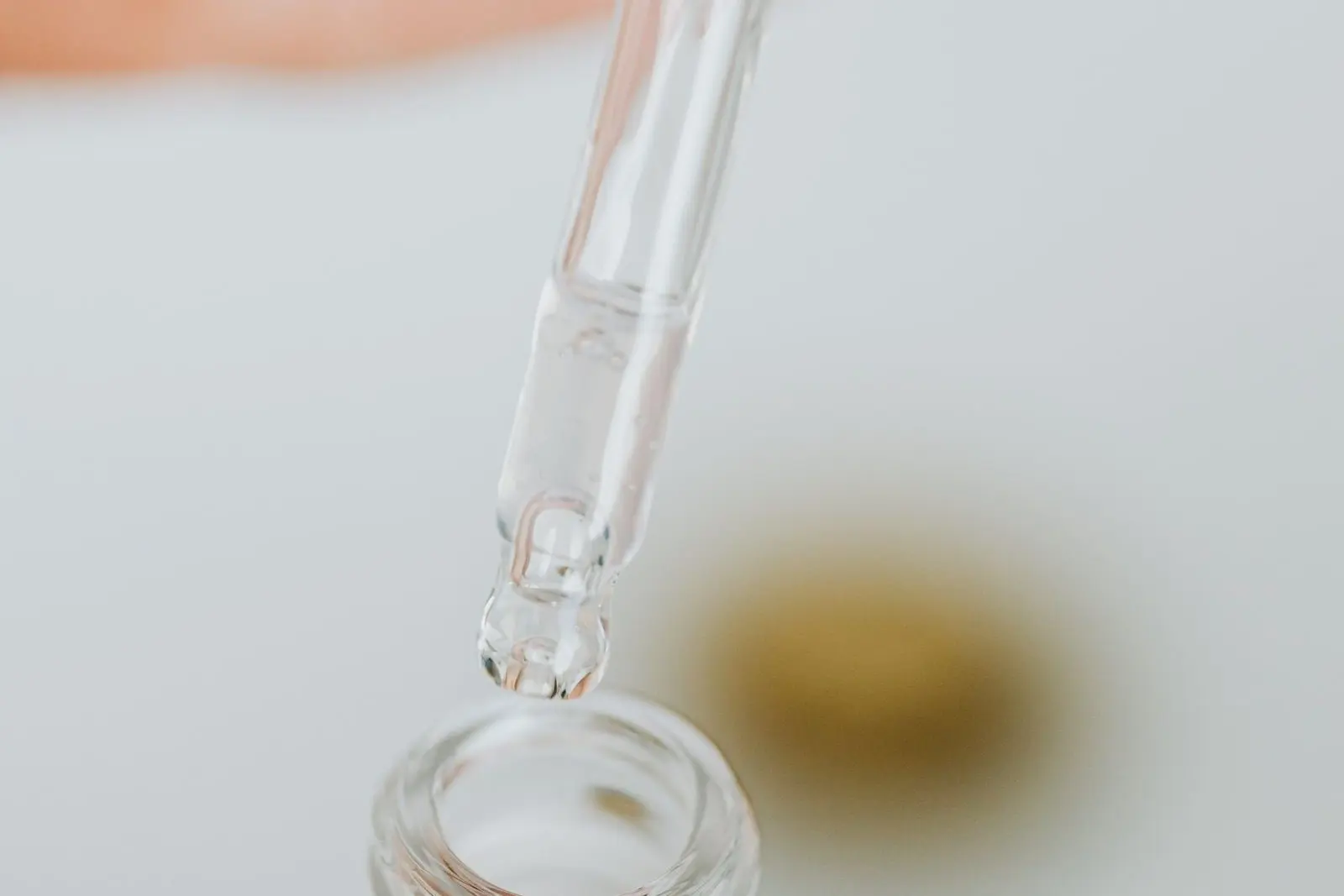Glass pipette above an open bottle, a drop about to fall