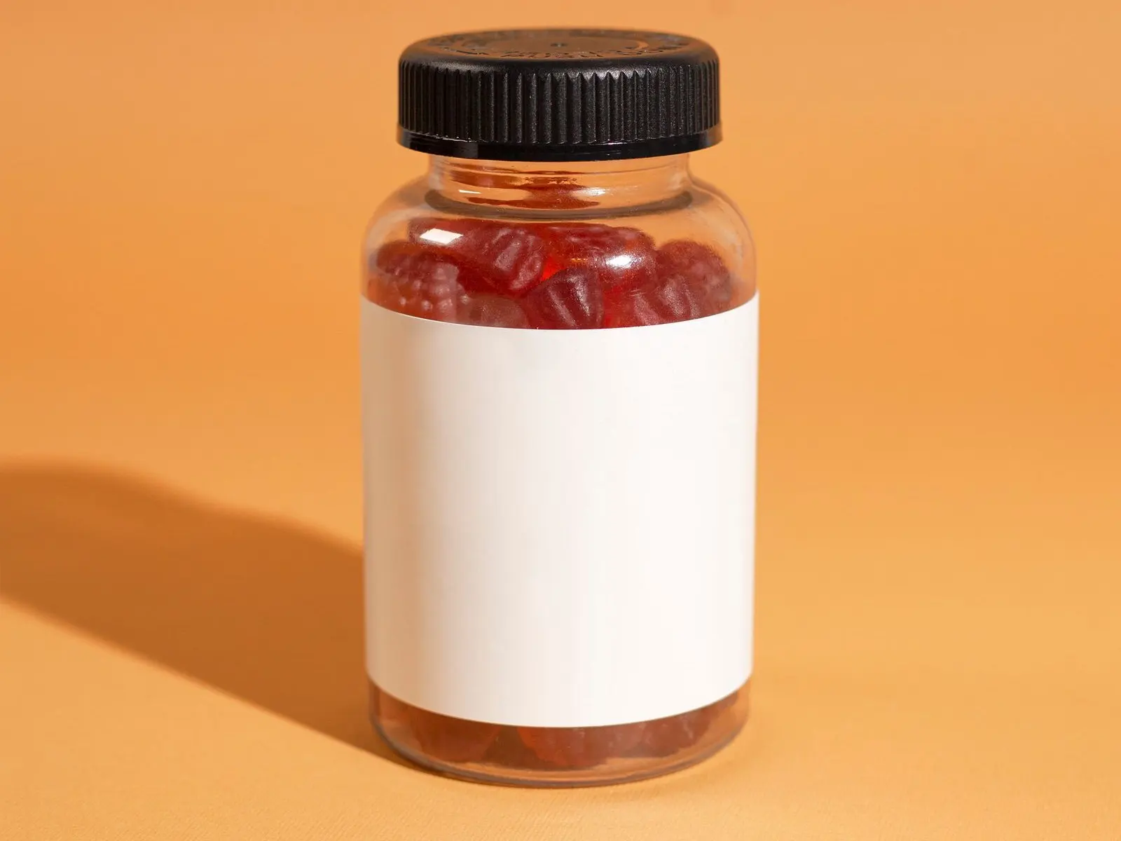 Clear jar filled with red gummies, blank label, on an orange background