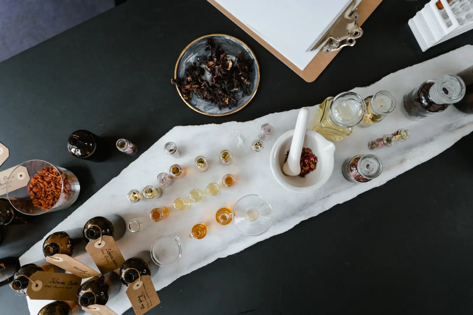 Amber and clear glass oil bottles, droppers and plant ingredients laid out on a table, seen from above