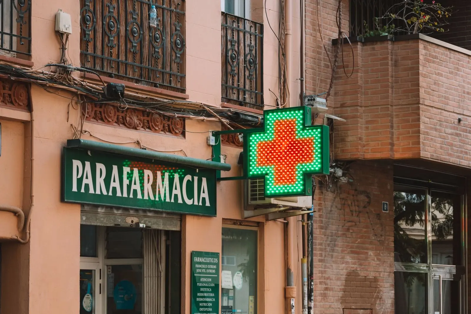 Illuminated green pharmacy cross and parapharmacy sign on a brick facade