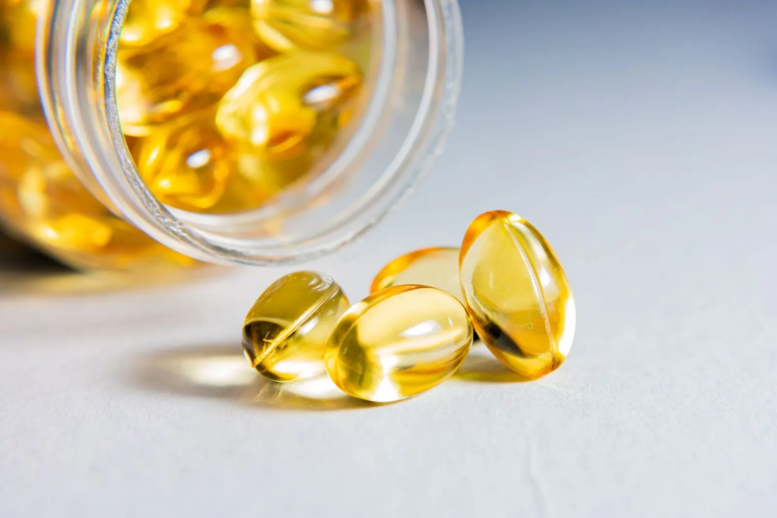 Clear oil-filled softgel capsules spilling from a glass jar