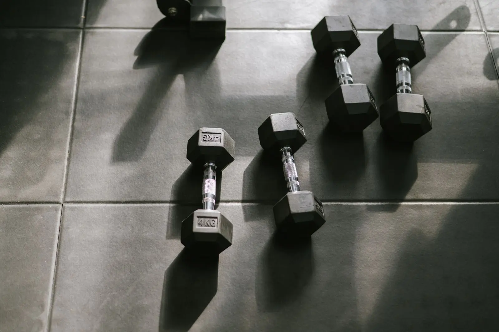 Hexagonal 4 kg dumbbells lying on a gym floor in low, raking light