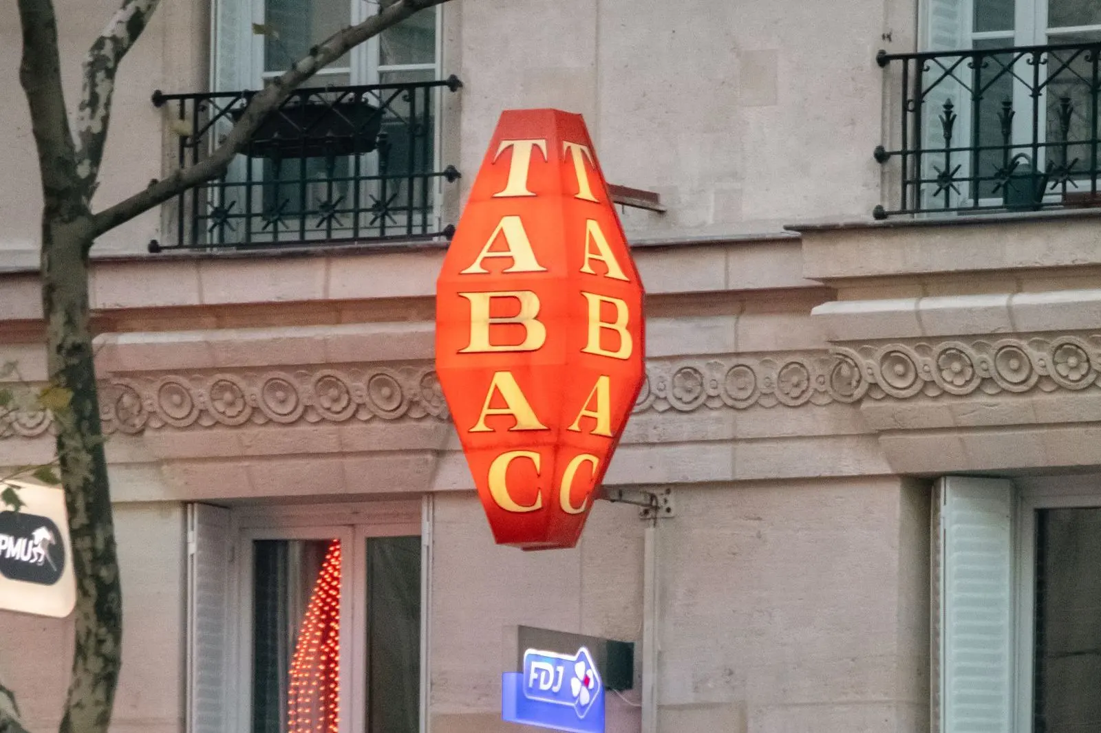 Red diamond-shaped “Tabac” sign on the front of a Parisian building