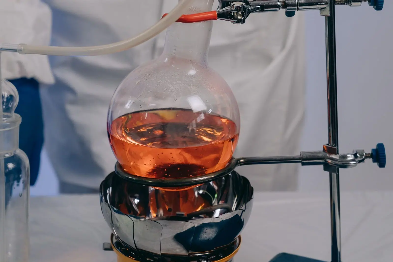 Laboratory flask filled with an orange liquid, sitting in a heating mantle and held by a clamp