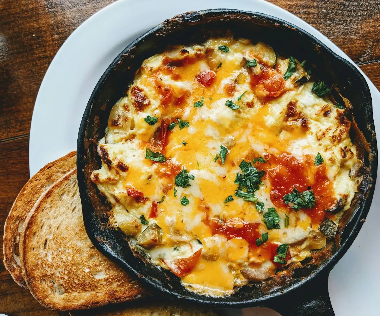 Baked omelette with tomatoes and parsley in a small cast-iron pan, served with two slices of toast