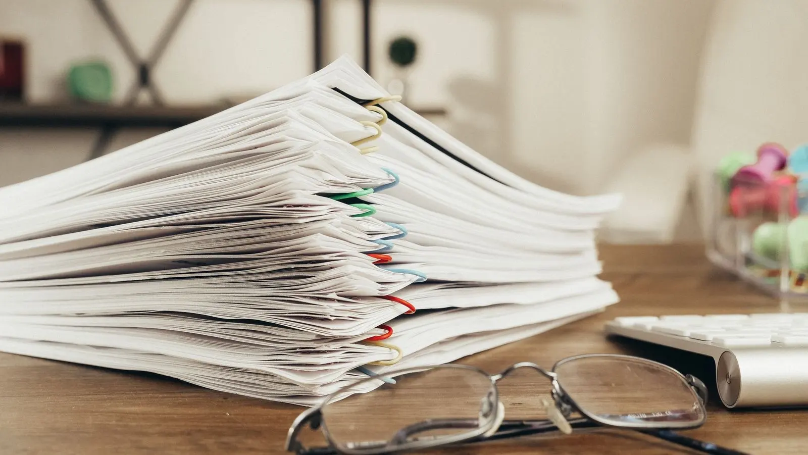 A stack of clipped documents on a desk, next to a pair of glasses