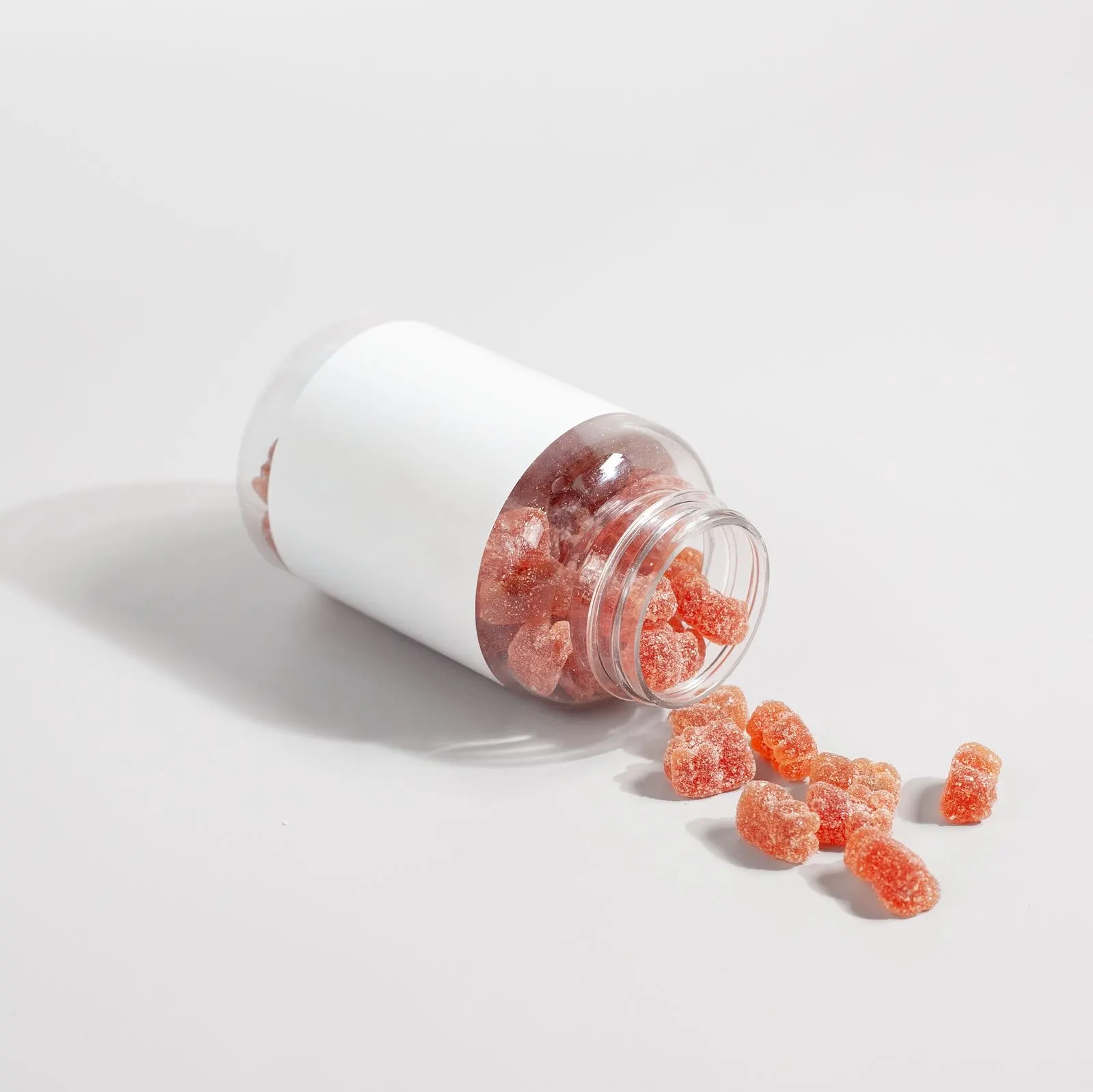 Unlabelled jar tipped over on a white table, spilling red sugar-coated gummies