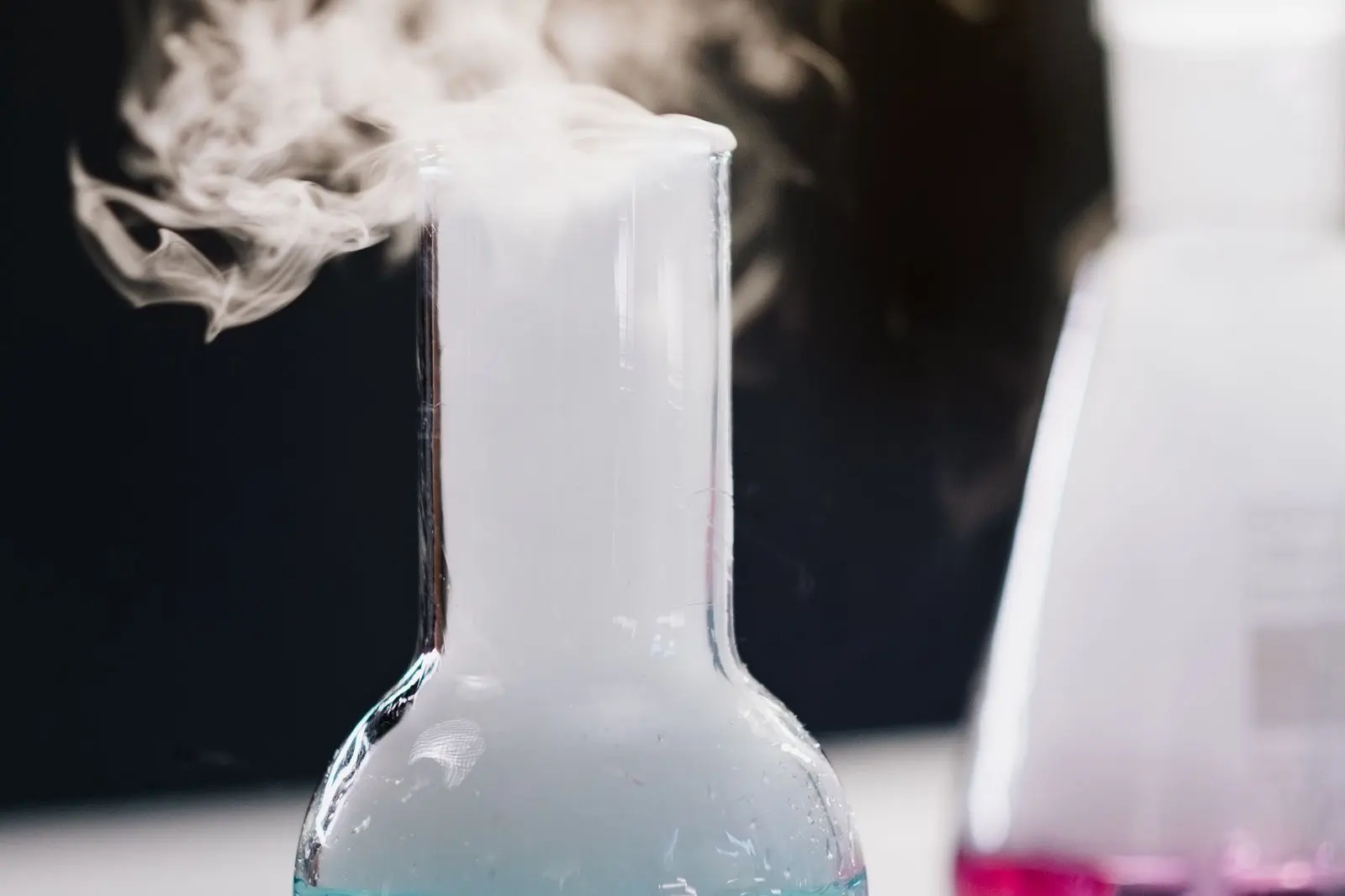 Laboratory flask releasing white vapour against a dark background